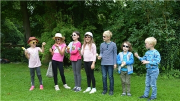 Sieben Kinder stehen auf einer Wiese.