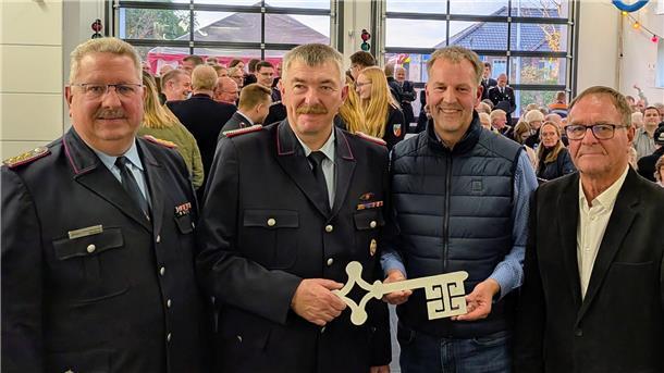 Große Freude in Appeln: Feuerwehr zieht in modernes Gerätehaus ein Vier Männer stehen bei der Einweihung eines Feuerwehrhauses zusammen, zwei von ihnen tragen Uniform. Einer hält einen symbolischen Schlüssel, im Hintergrund sind viele Gäste zu sehen.