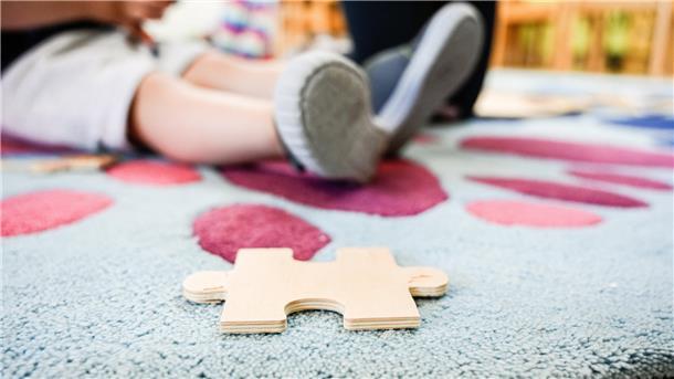 Ein Puzzleteil aus Holz liegt auf einem Teppich in einer Kita.
