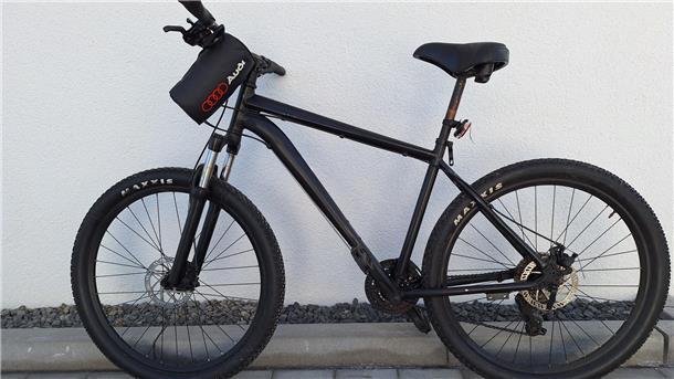 Ein schwarz lackiertes Fahrrad lehnt an einer weißen Wand. 