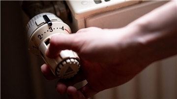 Jemand dreht am Thermostat eines Heizkörpers.