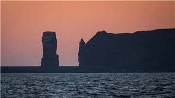 Schleswig-Holstein, Helgoland: Die Sonne geht hinter den Klippen von Helgoland auf.