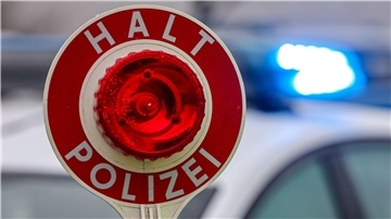 Ein Polizist hält eine Polizeikelle für eine Kontrolle in der Hand. 