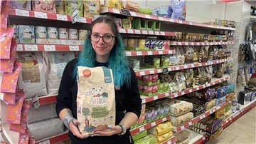 Eine Frau steht vor einem Regal mit Hundefutter. Sie hält einen Sack Trockenfutter in den Händen.