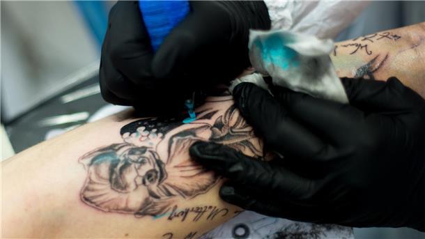 Tätowierer arbeitet an einem Arm. 