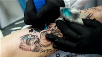 Tätowierer arbeitet an einem Arm. 