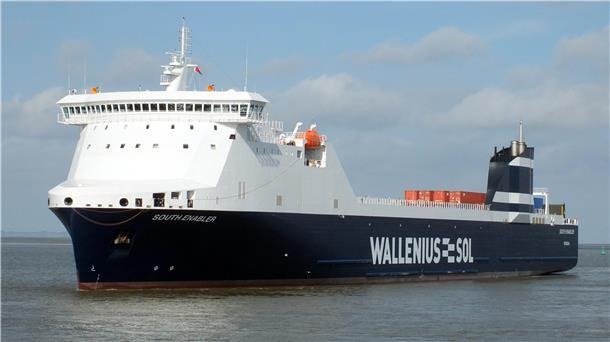 Ein großes, modernes RoRo-Frachtschiff mit dem Namen „South Enabler“ fährt bei Tageslicht auf ruhiger See. Der Rumpf ist dunkelblau mit dem weißen Schriftzug „Wallenius SOL“, das Steuerhaus und die Aufbauten sind weiß. Auf dem Deck stehen einige orangefarbene Container.