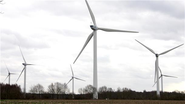 Mehrere große Windkraftanlagen stehen auf einem offenen Feld vor einem bewölkten Himmel. Im Hintergrund sind Bäume ohne Laub zu sehen. Die Szene wirkt ruhig und zeigt eine typische Landschaft mit moderner Windenergie-Nutzung.