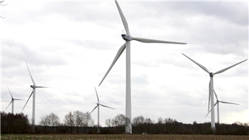 Mehrere große Windkraftanlagen stehen auf einem offenen Feld vor einem bewölkten Himmel. Im Hintergrund sind Bäume ohne Laub zu sehen. Die Szene wirkt ruhig und zeigt eine typische Landschaft mit moderner Windenergie-Nutzung.