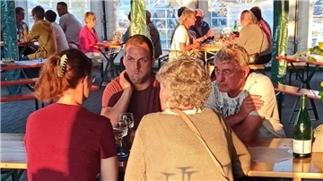 Besucher des Weinfestes sitzen in der Abendsonne an Tischen. 