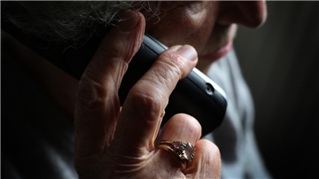 Eine ältere Dame hält sich ein Telefon ans Ohr.