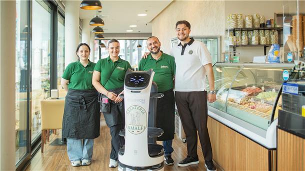 Drei Menschen stehen zusammen mit einem Service-Roboter vor einer Eistheke.