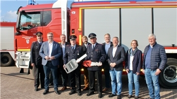 Landrat und Feuerwehrleute stehen vor einem Feuerwehrauto.