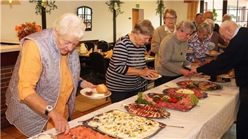 Senioren stehen vor der Tafel des Büfetts und füllen ihre Teller.