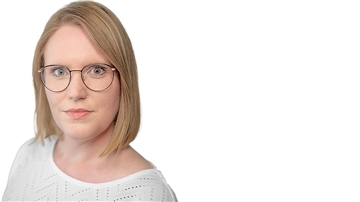 Blonde Frau mit dunkler Brille schaut direkt in die Kamera.