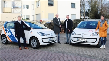 Das Foto zeigt vier Menschen und zwei Autos. Die beiden Herren geben sich die Hände.