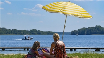 Eine Mutter und ihre Tochter sitzen unter einem Sonnenschirm im Strandbad am Storkower See.
