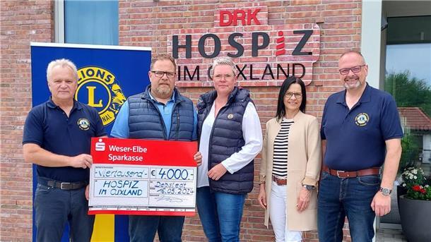 Vor einem Eingang mit dem Schriftzug "DRK Hospiz im Cuxland" stehen zwei Frauen und drei Männer nebeneinander. Zwei von ihnen halten einen symbolischen Spendenscheck über 4000 Euro.