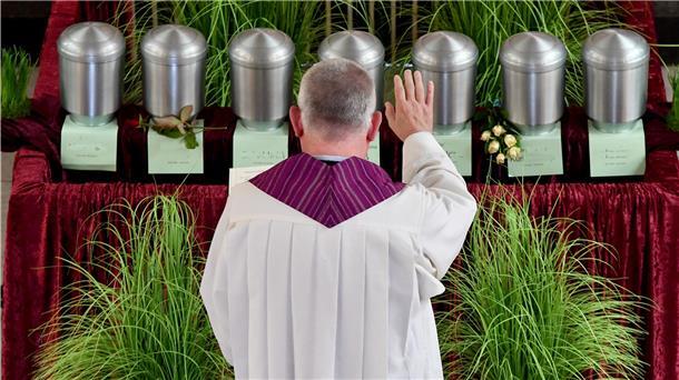 Ein Pastor steht vor sieben Urnen in einer Friedhofkapelle