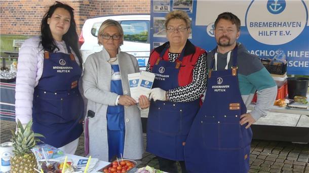 Drei Frauen und ein Mann stehen an einem Stand des Vereins "Bremerhaven hilft".