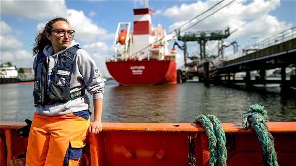 Frau steht vor Schiff.
