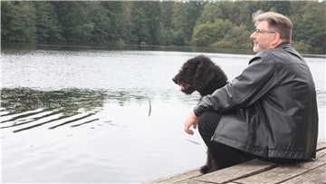 Ein Mann sitzt mit seinem Hund an einem See