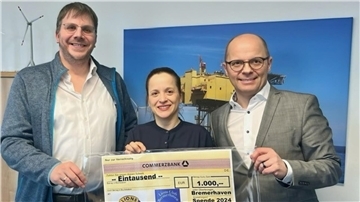 Drei Personen stehen nebeneinander und halten gemeinsam einen großen symbolischen Scheck über 1.000 Euro. Im Hintergrund ist ein Bild mit einer Offshore-Plattform und einer Windkraftanlage zu sehen.