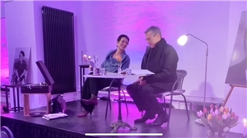 Ein Mann und eine Frau sitzen auf Stühlen an einem Tisch auf einer Bühne.