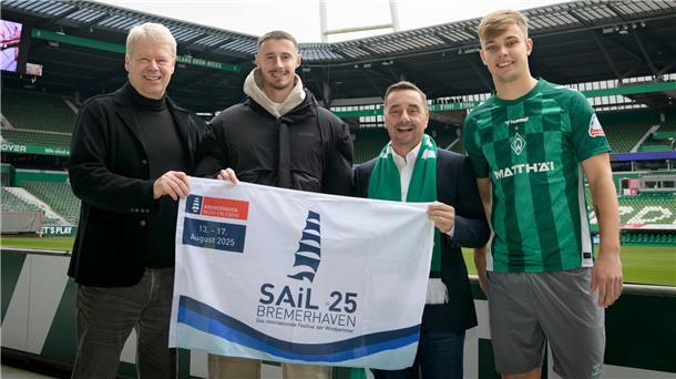 Von der Weser zum Windjammer: Werder Bremen unterstützt Sail Das Foto ist im Weserstadion entstanden, es zeigt vier Herren, die eine Flagge in der Hand halten, die auf die Sail 2025 hinweist. Freuen sich über die Partnerschaft: Dr. Ralf Meyer vom SAiL-Organisationskomitee, die Spieler Marco Friedl und Keke Topp sowie Michael Gerber, Geschäftsführer der Erlebnis Bremerhaven GmbH.
