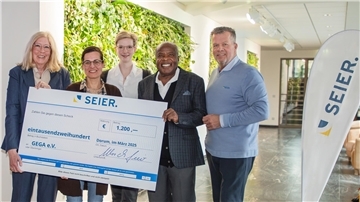 Fünf Personen stehen in einem modernen Innenraum mit begrünten Wänden und halten gemeinsam einen großen Spendenscheck der Firma SEIER über 1.200 Euro für den Verein GEGA e.V.