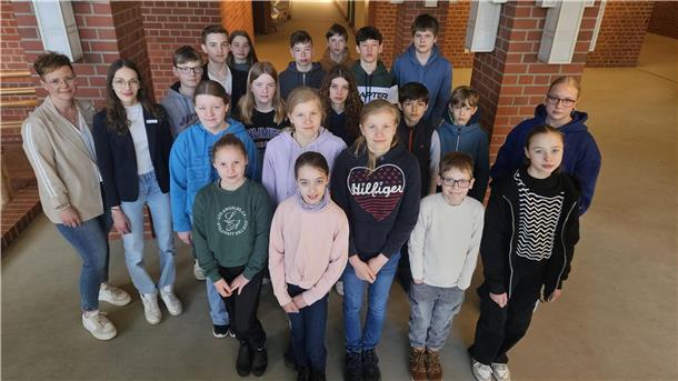 Eine Gruppe von rund 20 Personen, bestehend aus Schülerinnen und Schülern sowie zwei Frauen, steht im Flur eines Verwaltungsgebäudes vor einer Backsteinwand.