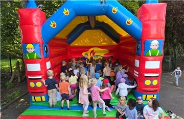 Zahlreiche Kindergartenkinder spielen fröhlich in einer bunten Hüpfburg mit Feuerwehrmotiv auf dem Außengelände des EWW Kindergartens Nimmerland.