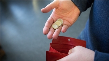 Eine Hand mit drei Münzen über einem leeren Portemonnaie.