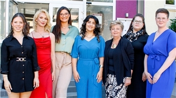 Sieben Frauen stehen in festlicher Kleidung vor einem Gebäude und lächeln in die Kamera.