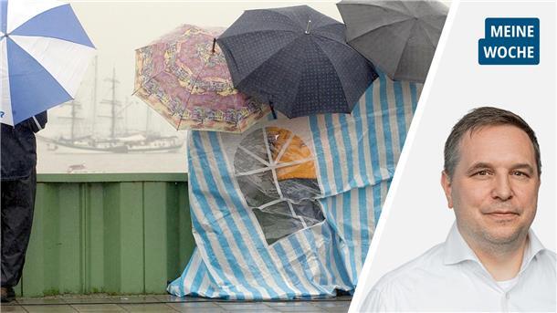 Menschen schützen sich mit Schirmen und Planen vor Regen, im Hintergrund ein Segelschiff.