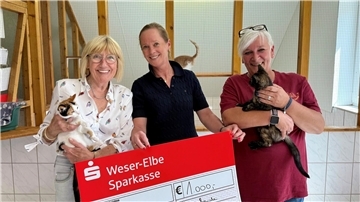 Drei lächelnde Frauen mit Katzen und Riesenscheck