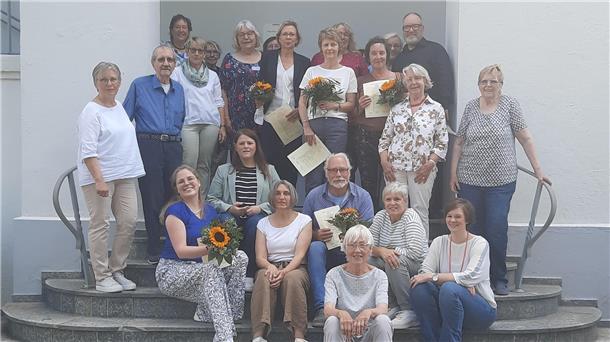 Hombre qualifiziert Hospizbegleiter  Menschen stehen vor einem Gebäude und halten Zertifikate und Blumen in der Hand.