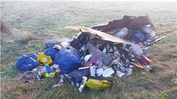 Ein Haufen illegal entsorgter Abfälle liegt auf einer Wiese. Zu sehen sind blaue und gelbe Müllsäcke, Holzreste, Plastikgeschirr, Unrat und Hausmüll.