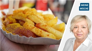 Eine Hand hält eine Portion Currywurst mit Pommes