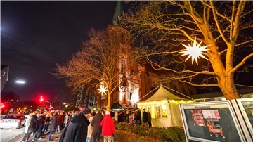 Viele Menschen vor einer Kirche und Weihnachtsbeleuchtung an Bäumen. 
