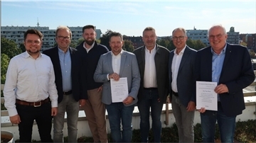 Gruppenbild mit sieben Männern. Zwei von ihnen halten eine Urkunde in den Händen.