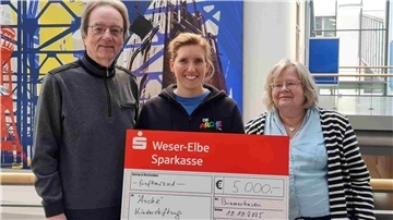 Ein Mann und zwei Frauen mit einem Riesenscheck