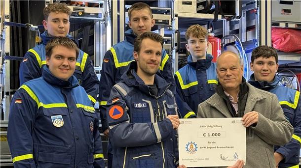 Zwei Männer aus einer Gruppe halten einen großen Scheck.