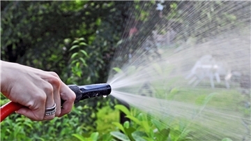 Eine Hand hält einen Gartenschlauch, aus dem Wasser spritzt.