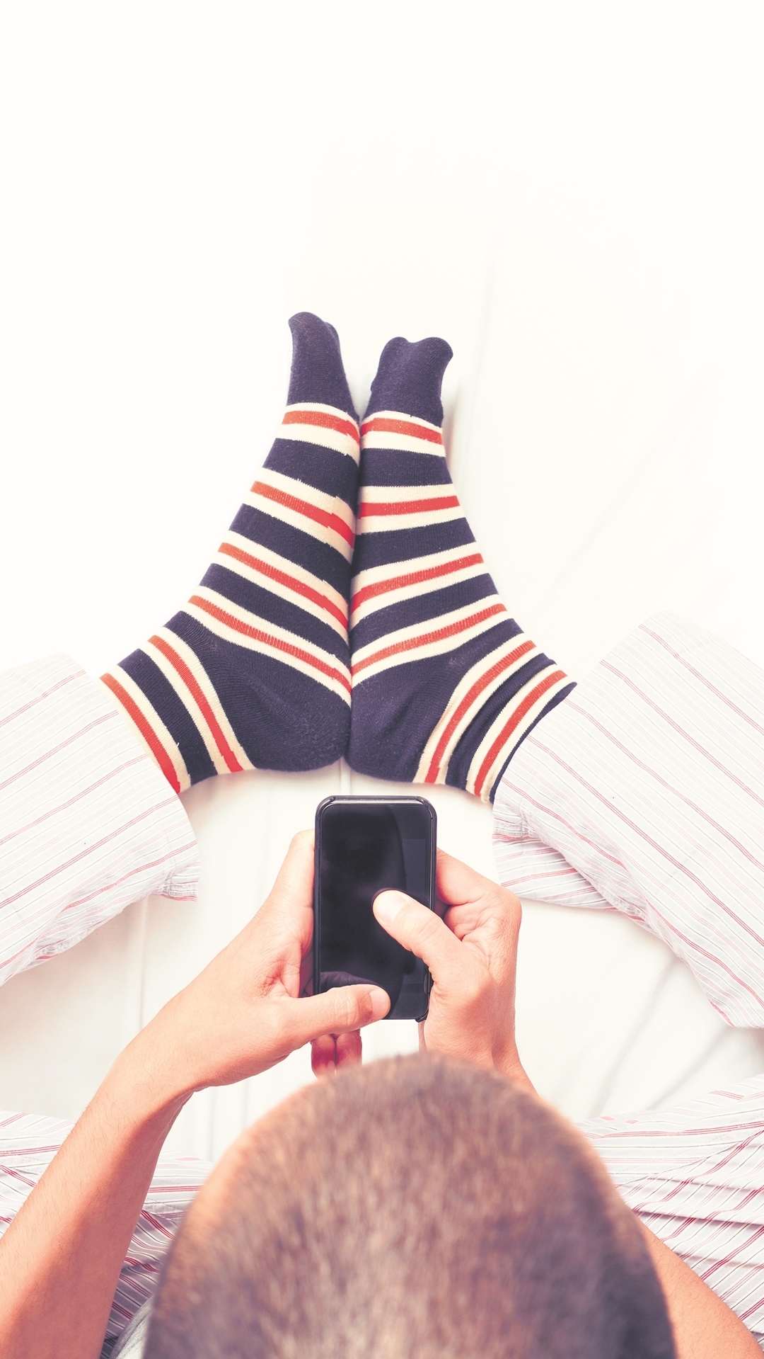 Ein Mann sitzt mit seinem Handy im Bett