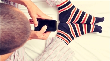 Ein Mann sitzt mit seinem Handy im Bett