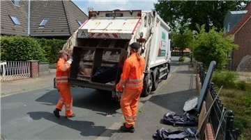 Zwei Männer in Arbeitskleidung tragen ein altes Regal in den Sperrmüllwagen.