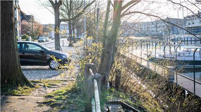 Blick auf die Kaistraße mit Bootsanlegestelle und Parkplätzen neben Wohn- und Geschäftsgebäuden.