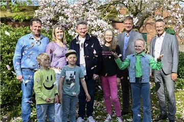 Gruppenfoto mit Erwachsenen und Kindern im Grünen. Blütenkonfetti für ein Vierteljahrhundert Opernkult (von links): Gastgeber Sönke und Sunhild Holsten, Adrian Rusnak (musikalischer Leiter), Moderatorin Martina von Ahsen, Carsten Hoops vom Niedersächsischen Landvolk und Stefan Hunsche vom Vorstand der Bremischen Volksbank Weser-Wümme freuen sich auf die nächste Auflage.