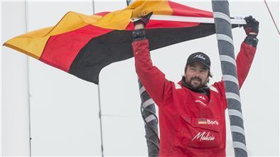 Boris Herrmann, Skipper aus Deutschland, jubelt mit einer Fahne auf seiner Jacht «Seaexplorer - Yacht Club de Monaco» bei der neunten Auflage der Vendee Globe Weltumsegelung 2020/2021 nachdem er vor der Küste von Les Sables d'Olonne die Ziellinie überquert hat. 